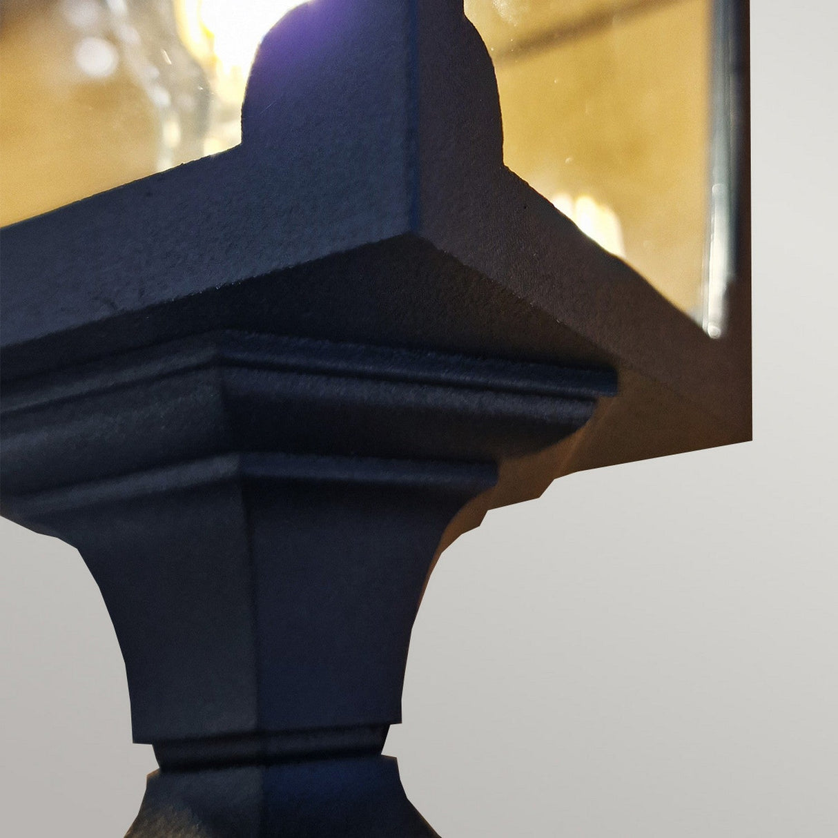 A close-up of the Chapel 1 Light Lamp Post in black showcases its angular design crafted from die-cast aluminum, featuring a reflective glass panel that casts a soft light. Its modern geometric style stands out against a plain background, making it an ideal choice for stylish outdoor lighting.