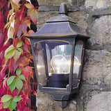 The Chapel-1 1 Light Outdoor Wall Lantern - Black is a vintage-looking die-cast aluminum fixture mounted on a stone wall, surrounded by vibrant red and green climbing leaves. It features a glowing bulb inside and boasts an IP44 rating for durability.