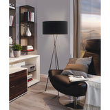 Crelvane Floor Lamp in black, tripod steel legs with a wide fabric drum shade, shown beside an armchair in a living room setting.