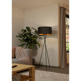 Crelvane Floor Lamp in black, a tripod design with slim steel legs and a wide fabric drum shade with copper-lined interior, shown in a living room setting.