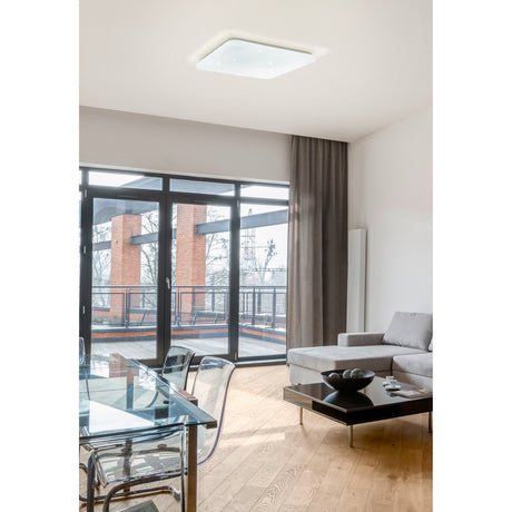 Crelvette square LED ceiling panel light, 43 x 43cm, white steel body with crystal-effect diffuser, shown flush-mounted on a living room ceiling above a lounge and dining area.