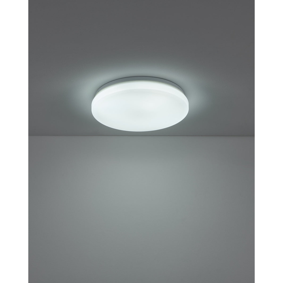 Crelvette LED Bathroom Ceiling Light 31cm in white, round flush fitting with plastic diffuser glowing on a grey ceiling, IP44 rated, shown installed in a plain room setting.