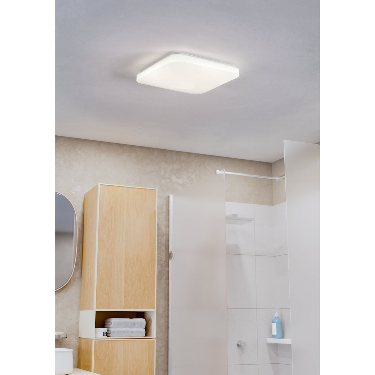 Crelvette LED Bathroom Ceiling Light, a square white flush fixture with softly rounded corners, shown mounted on a bathroom ceiling above a timber storage unit and shower screen.