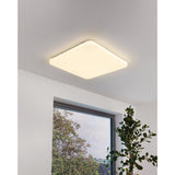 Crelvette 53 x 53cm square LED ceiling panel light in white, mounted flush on a bedroom ceiling with warm white glow, shown near a window and plant.