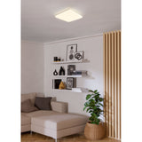 Crelvette 53 x 53cm square LED ceiling panel light in white, mounted flush on a living room ceiling above shelving, a sofa, and a potted plant.