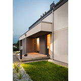 Cronvena Outdoor LED Floor Lamp in black, slim bollard-style posts with illuminated white diffuser heads, shown either side of a modern house entrance at dusk.