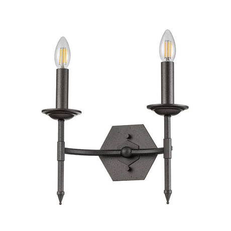 The Crown 2 Light Wall Light - Graphite is a wall-mounted sconce with an antique-style design that exudes timeless elegance. It features a graphite finish and has two upward-facing candle-like arms topped with clear bulbs, set against a hexagonal backplate. This piece elegantly combines classic and industrial elements.