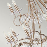 A close-up of the Christina 18 Light Chandelier, featuring elegant curved arms with crystal drops and small candle-shaped light bulbs. The chandelier's silver and gold patina shines beautifully against a soft gradient background, accentuating its intricate details.