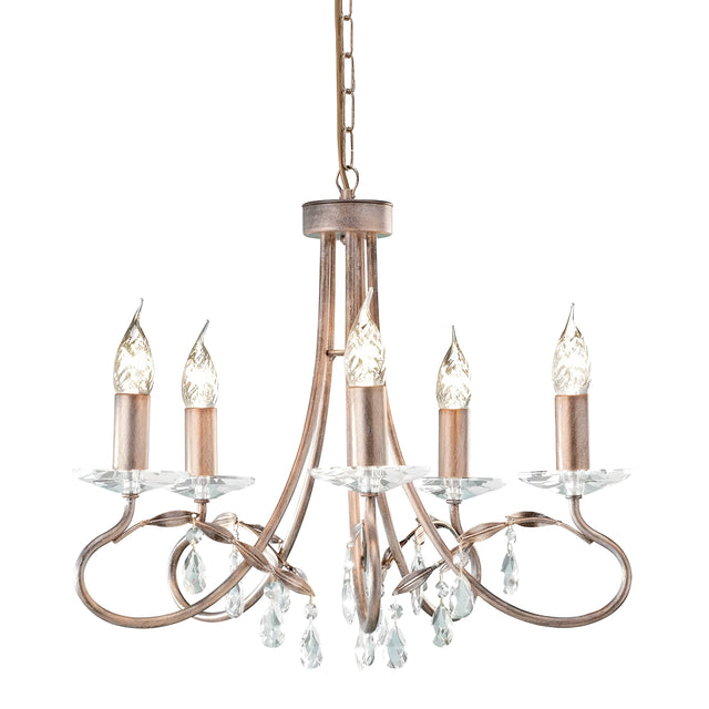 Introducing the Christina 5 Light Chandelier in Silver/Gold Patina, featuring a vintage style with five candle-shaped lights adorned with crystal drops. The chandelier boasts a bronze finish, elegantly curved metal arms, and hanging droplets, all suspended from a chain. The bulbs are designed to resemble flames, adding an elegant touch to this convertible design fixture.