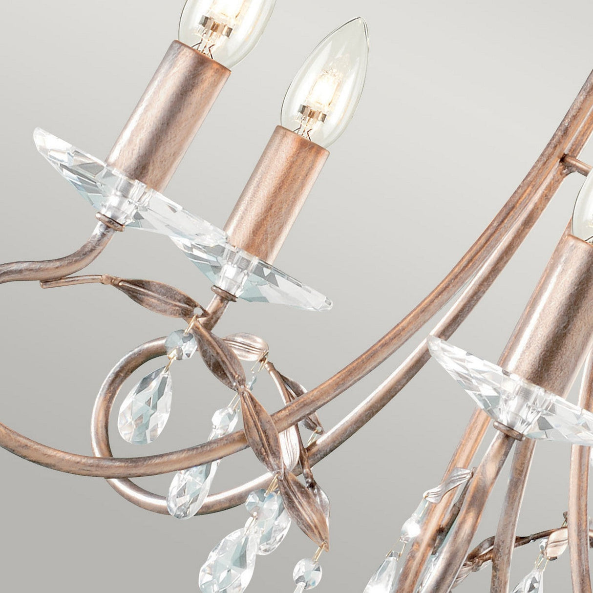 A close-up of the Christina 5 Light Chandelier in Silver/Gold Patina showcases its candle-shaped bulbs, ornate curved metal arms, and crystal drops suspended elegantly against a neutral background.