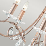 A close-up of the Christina 5 Light Chandelier in Silver/Gold Patina showcases its candle-shaped bulbs, ornate curved metal arms, and crystal drops suspended elegantly against a neutral background.
