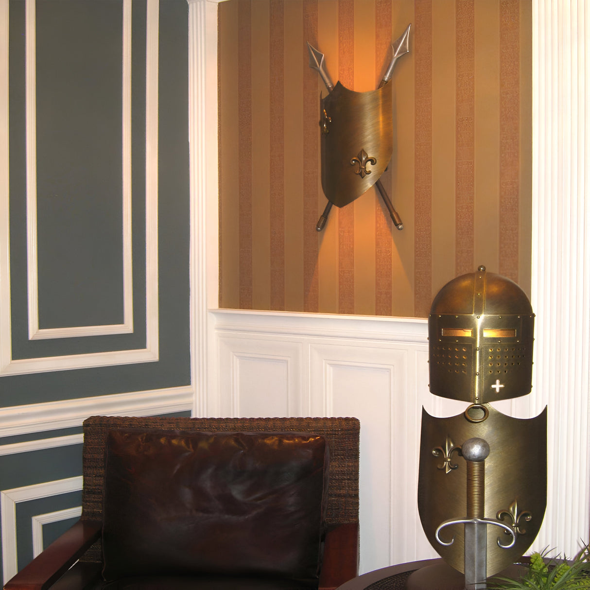 A corner of the room exudes a medieval ambiance with a dark leather chair, a decorative shield featuring crossed spears on a striped wall, and the helmet and chest plate of a suit of armor adorned with fleur-de-lis designs. The Crusader Wall Light in burnished bronze casts a subtle glow over the display.