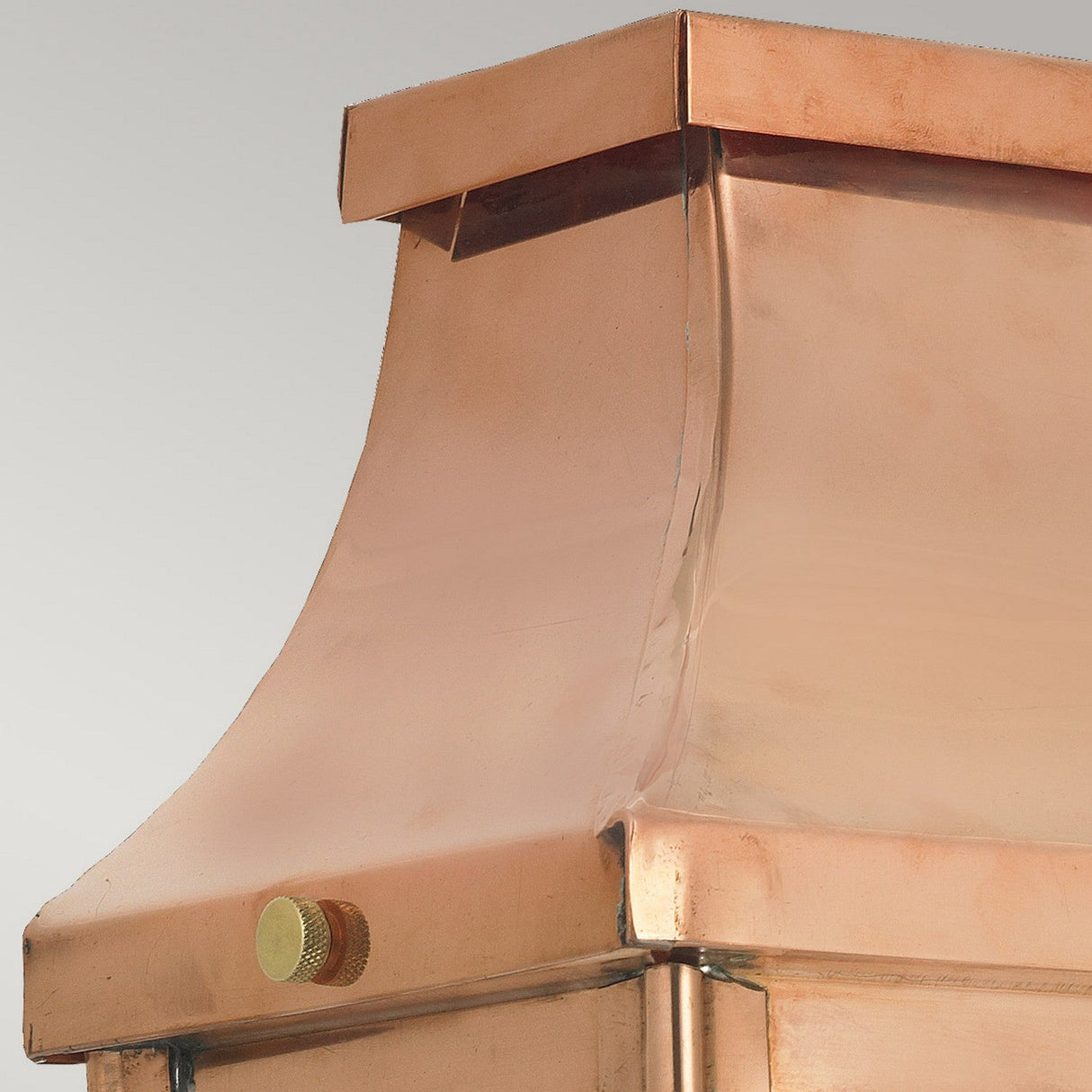 A close-up view of the Chelsea Outdoor 1 Light Large Half Lantern - Copper reveals its elegantly smooth, curved design that resembles a copper chimney cap. The polished metallic surface reflects light brilliantly, and a small round adjustment knob on one side stands out against the neutral gray background, enhancing the lantern's elegance.