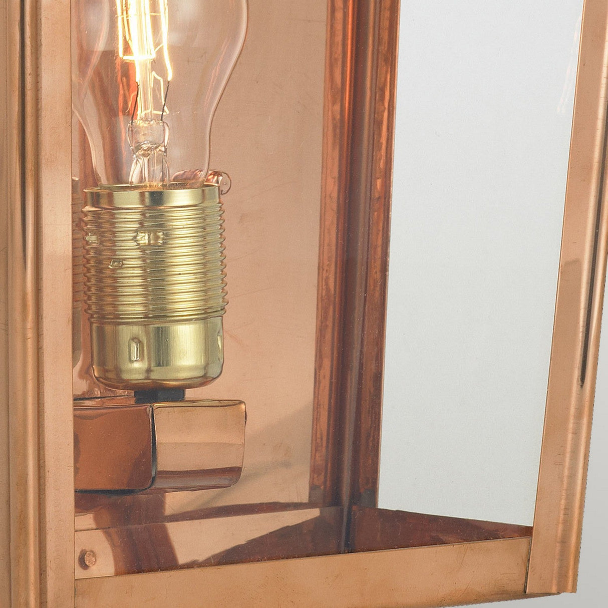 The Chelsea Outdoor 1 Light Large Half Lantern - Copper, featuring a vintage-style light bulb with a brass base, elegantly showcases the bulb's intricate details while its weather-resistant design beautifully reflects light.