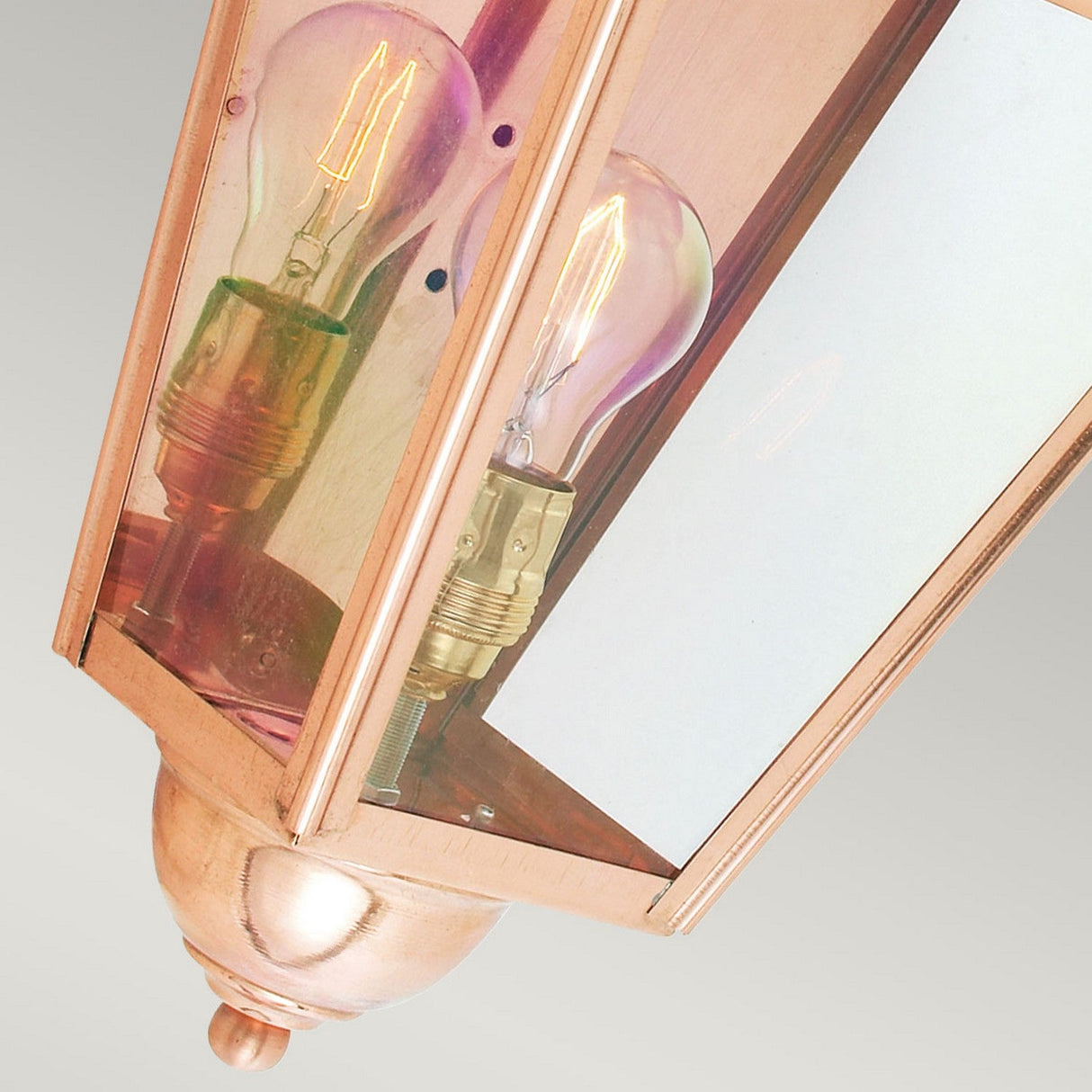 This close-up of the Chelsea Outdoor 1 Light Half Lantern in copper spotlights an exquisite outdoor lighting fixture. Its traditional hexagonal design, combined with clear glass panes, highlights a visible filament bulb inside. As time passes, the lantern's patina finish will enhance its charm while mounted against a neutral background.