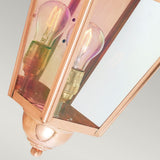 This close-up of the Chelsea Outdoor 1 Light Half Lantern in copper spotlights an exquisite outdoor lighting fixture. Its traditional hexagonal design, combined with clear glass panes, highlights a visible filament bulb inside. As time passes, the lantern's patina finish will enhance its charm while mounted against a neutral background.