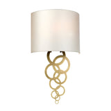 The Curtis Medium Wall Light - Aged Brass is designed with a sleek white cylindrical shade and stylish aged brass interlocking rings. Its contemporary design effortlessly complements different interior styles, bringing a touch of sophistication to any room.