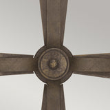 A close-up of a metallic ceiling fan highlights three angular blades converging at a central circular hub, set against a light gray background. The fan's textured design, reminiscent of the Cromwell 2 Light Wall Light in Old Bronze, exudes an industrial charm with its weathered medieval inspiration.