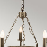 The Cromwell 5 Light Chandelier in Old Bronze showcases a close-up of its three lit candle-shaped bulbs and elegant metal chains, all with a bronze finish that evokes a medieval-inspired design, set against a gray background.