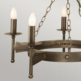 Boasting a medieval-inspired design, the Cromwell 5 Light Chandelier - Old Bronze features a circular metal frame adorned with three candle-shaped light bulbs. Suspended by sturdy metal chains against a light gray background, its handcrafted iron details embody elegance reminiscent of vintage style.