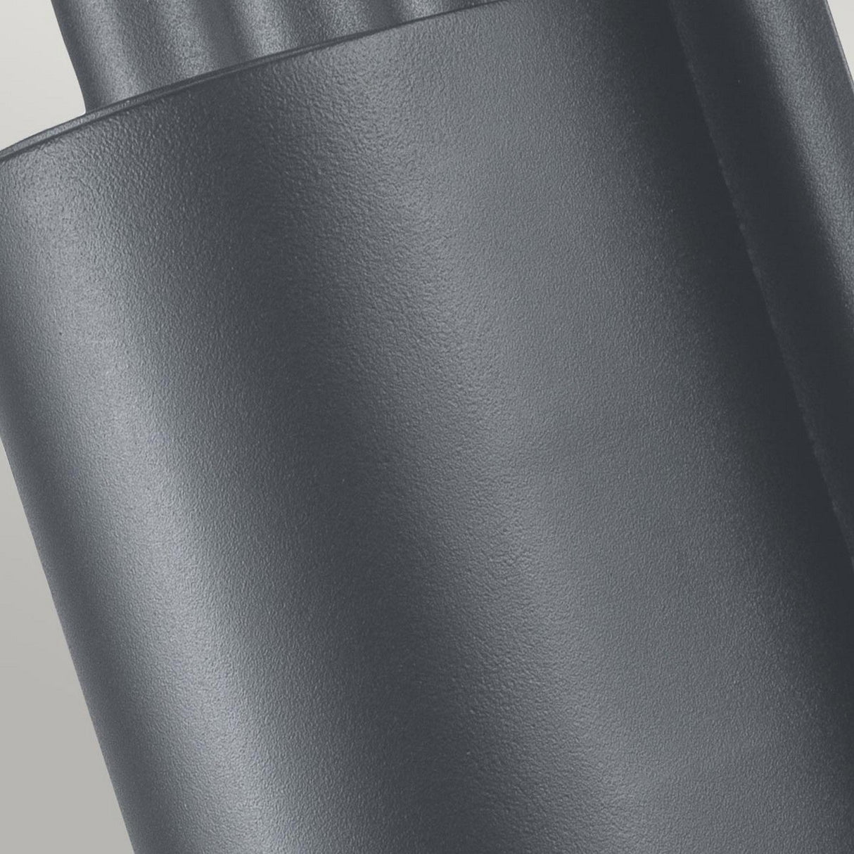Close-up of the Dali Outdoor Wall Light in gray, featuring a textured cylindrical shape with vertical grooves. Its matte finish reflects its durable stainless steel construction. Lighting and shadows accentuate the minimalistic design against a soft, light gray background.