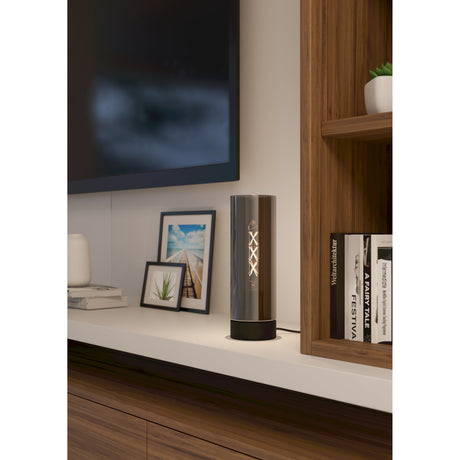 Damasco 1 Table Lamp in black, a slim smoked glass cylinder on a round black steel base, shown lit on a shelf beside framed photos and books.