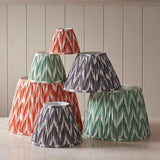 Endon Daneton tapered lamp shades in green, apricot orange and grey zigzag pleated faux silk, grouped on a pale surface against a neutral panelled wall.
