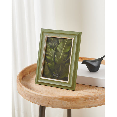 Dawanli Photo Frame in sage green with stepped moulding and pale gold inner lip, displaying a leaf print, standing on a wooden side table.