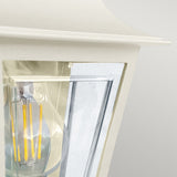 Close-up of the Deco Outdoor Wall Lantern with a visible clear glass bulb and yellow filaments. It features a modern lantern design with a cream finish and sleek glass panels, enhancing its contemporary appeal.