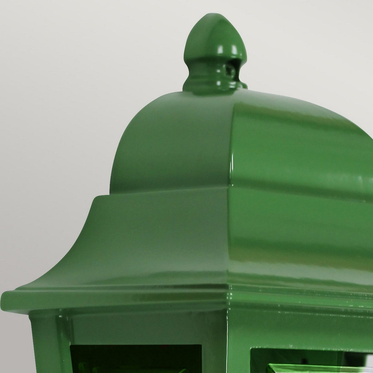Close-up of the Deco Outdoor Wall Lantern - Green against a neutral background. This vintage-style decorative lighting piece features a smooth, glossy finish with distinctive curved top details, reminiscent of classic streetlamp designs. Ideal for adding charm to any outdoor setting.
