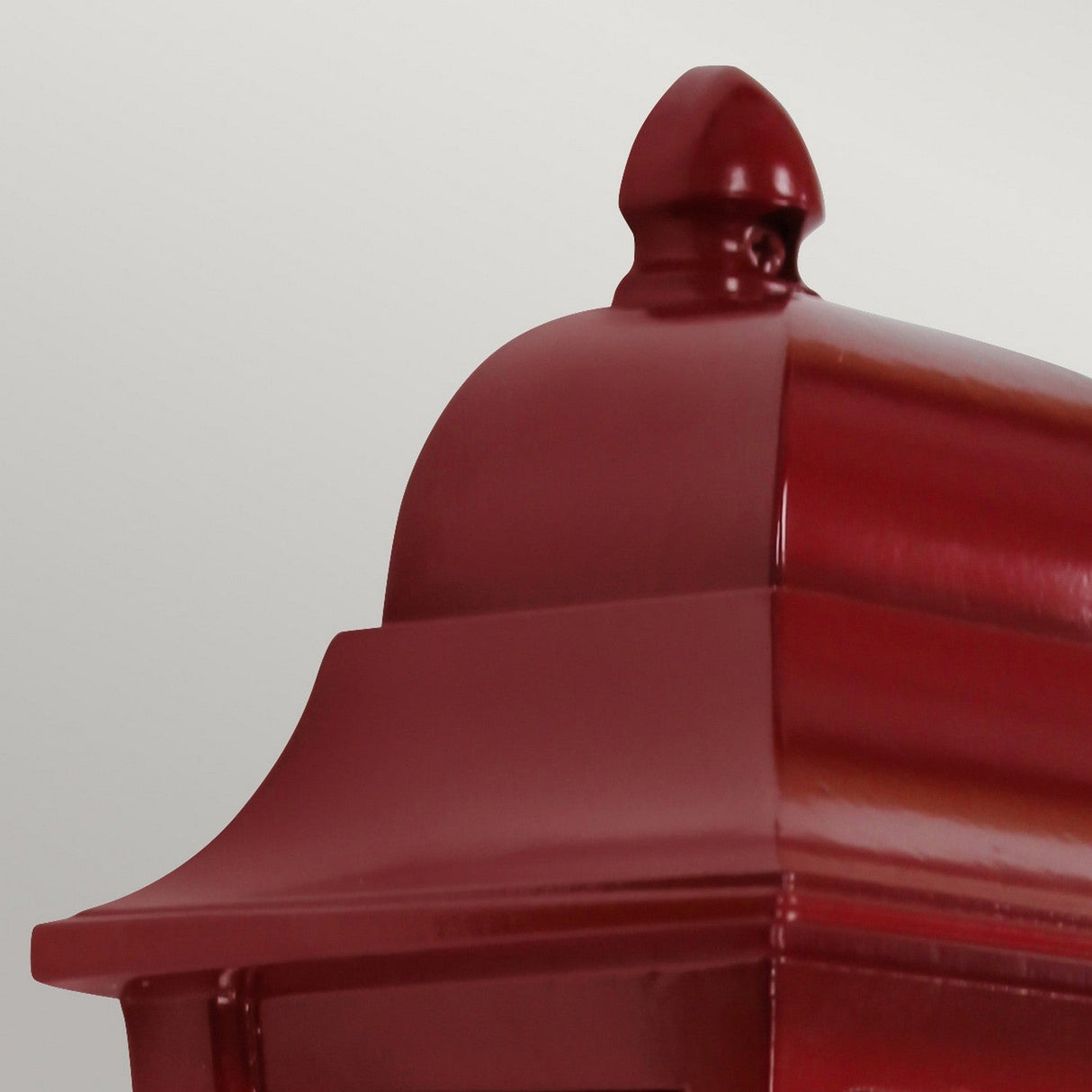 A close-up of the shiny Deco Outdoor Wall Lantern - Red reveals its striking dark red finish, featuring a smooth, curved top and a small finial. Crafted from aluminum for added durability, the lantern's mirrored backplate enhances its reflective shine against the plain light gray background.