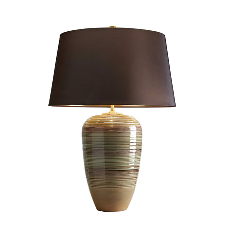 The Demeter Table Lamp - Green & Brown Glaze features an oval-shaped ceramic base with earthy tones and horizontal stripes, enhanced by a reactive glaze finish. Accompanied by a large dark brown lampshade, it provides a modern and stylish ambiance.