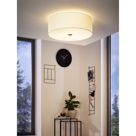 Dernessa 3 Light Ceiling Light in white fabric drum with satin nickel finial, shown flush-mounted in a corner room setting with a wall clock, plant, and side table.