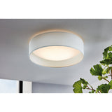 Dernessa LED Flush Ceiling Light in white, a round fabric drum shade with white diffuser, shown mounted on a ceiling beside green foliage.