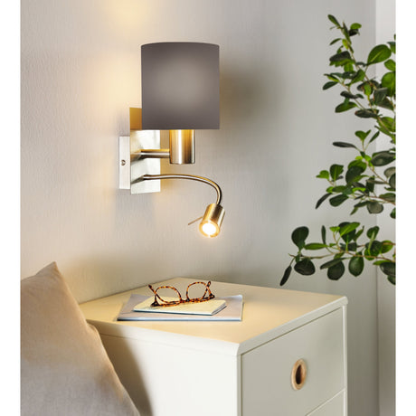Dernessa LED Wall Light with anthracite drum fabric shade and satin nickel body, flexible reading arm lit beside a bedside chest in a bedroom setting.
