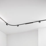 Deva 1m Surface 24V Lighting Track in black, shown curving across a white ceiling fitted with black spotlights and a linear light insert.