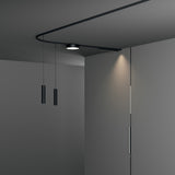 Deva 2m Surface 24V Lighting Track in black, shown curving along a grey ceiling with a round spotlight and two slim pendant lights suspended nearby.