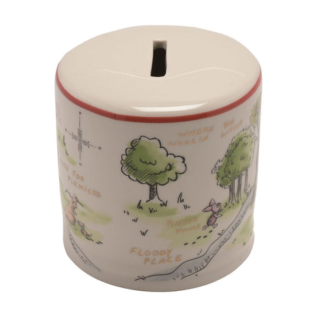 Round white ceramic money box with a coin slot lid, featuring a hand-drawn Winnie the Pooh map design with trees, Piglet, and orange place names on a plain background.