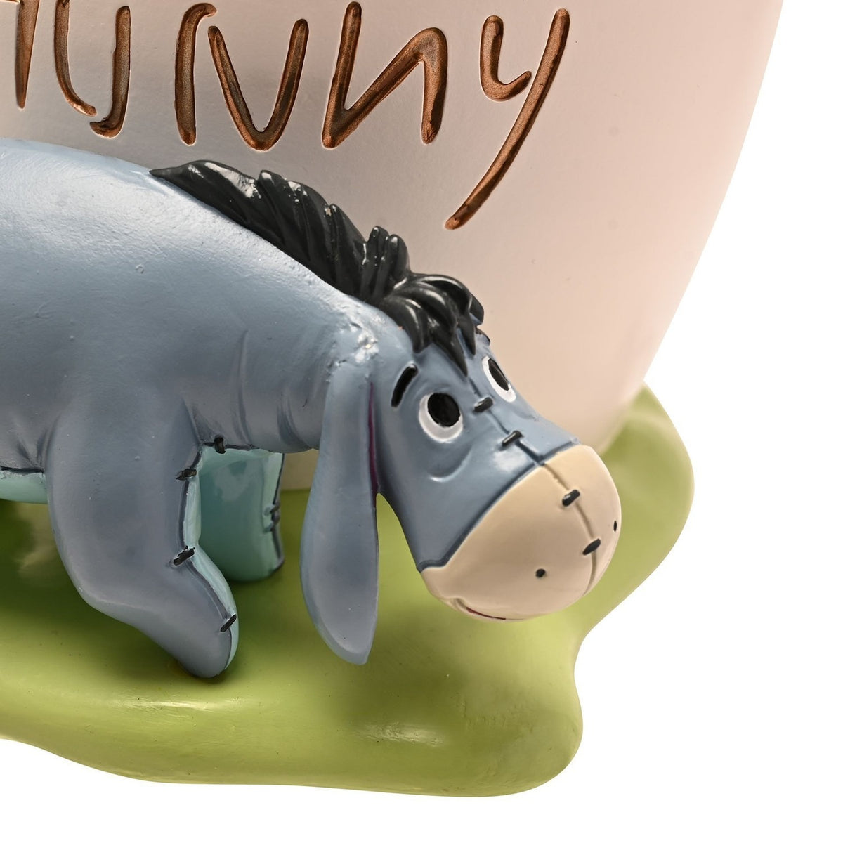 Close-up of the Winnie the Pooh resin Hunny Pot money box showing Eeyore figure on green grass beside the white pot engraved "Money for Hunny" with honey drips.