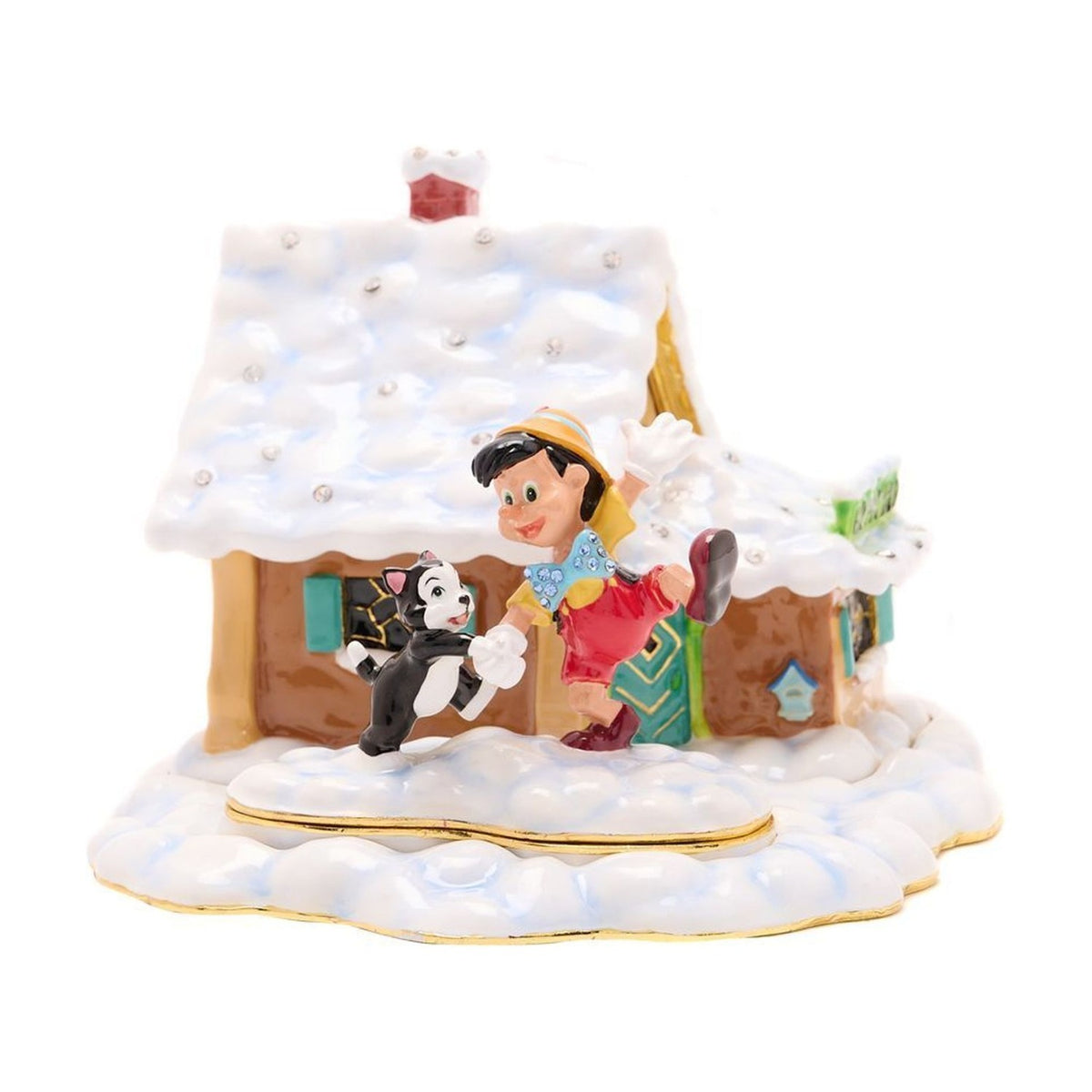 Metal trinket box shaped as a snow-covered cottage with tan walls, teal shutters and door, Pinocchio in yellow hat and red shorts dancing with Figaro the kitten outside, on a plain white background.