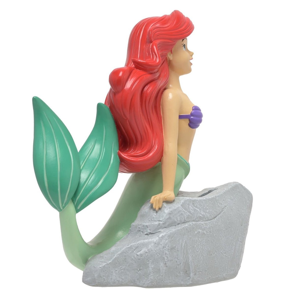 Resin money box of Ariel the mermaid leaning on a textured grey rock with coin slot, red hair, purple shell top, green tail, on a plain white background.