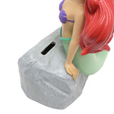 Close-up of the Ariel Mermaid resin money box showing her arm resting on the textured grey rock with the coin slot, green tail and red hair visible.