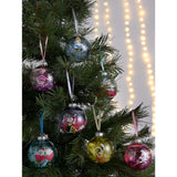 Seven round glass Christmas baubles in different colours on a tree, each featuring an Alice in Wonderland character including Alice, Mad Hatter, Cheshire Cat, and Queen of Hearts.