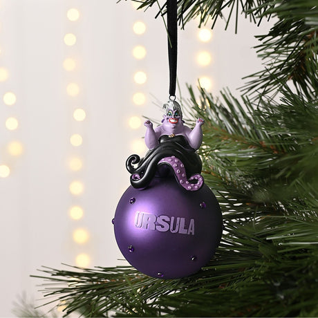 Ursula on Glass Bauble Christmas Tree Decoration in purple, with figure perched atop a studded round bauble reading "URSULA", hung from a black ribbon on a Christmas tree.