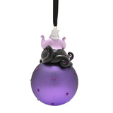 Glass Christmas bauble ornament featuring Ursula with white hair and black tentacles seated atop a round purple bauble studded with small purple gems, hung from a black ribbon on a white background.