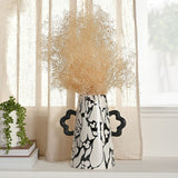 Large ceramic vase with black marbled Mickey Mouse pattern on speckled white, tapered body and wavy black handles, holding dried grasses on a living-room sideboard.