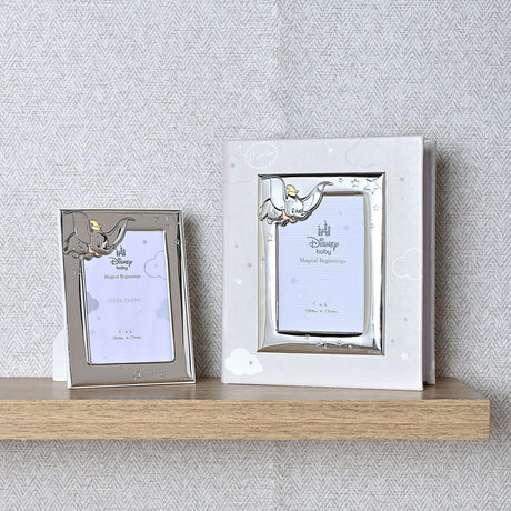 Dumbo Photo Album with silver metal Dumbo frame and grey cover, holding a 6 x 4in photo, shown beside a smaller matching Disney Baby photo frame on a wooden shelf.