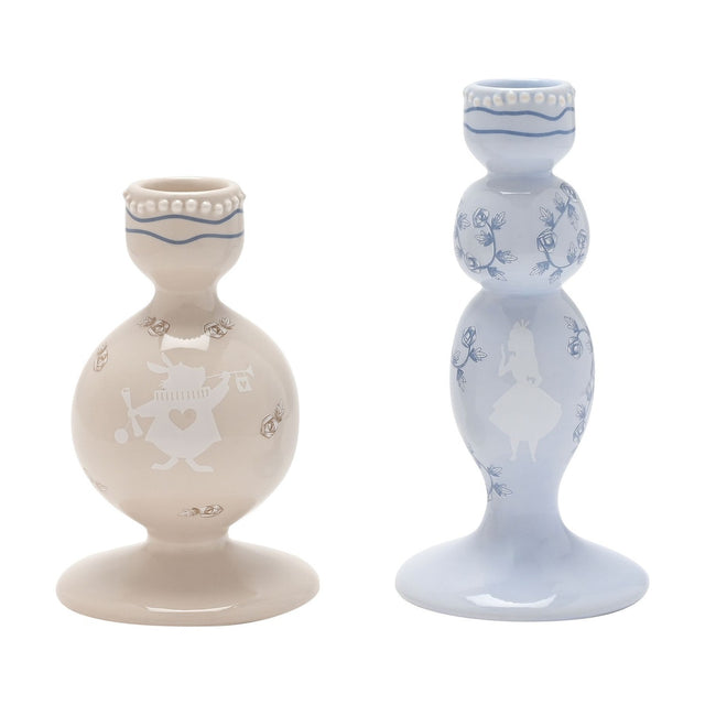 Set of two ceramic taper candle holders, a beige tiered holder with a White Rabbit silhouette and a taller pale blue holder with an Alice silhouette and rose detailing, on a white background.