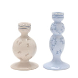Set of two ceramic taper candle holders with tiered pedestal bases, one pale blue with rose vine detailing, the other beige with scattered floral motifs.