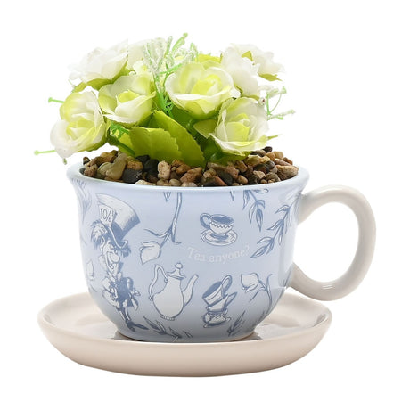 Alice in Wonderland ceramic teacup planter in pale blue with Mad Hatter and teapot print, holding a faux white and green rose plant, set on a beige saucer against a white background.